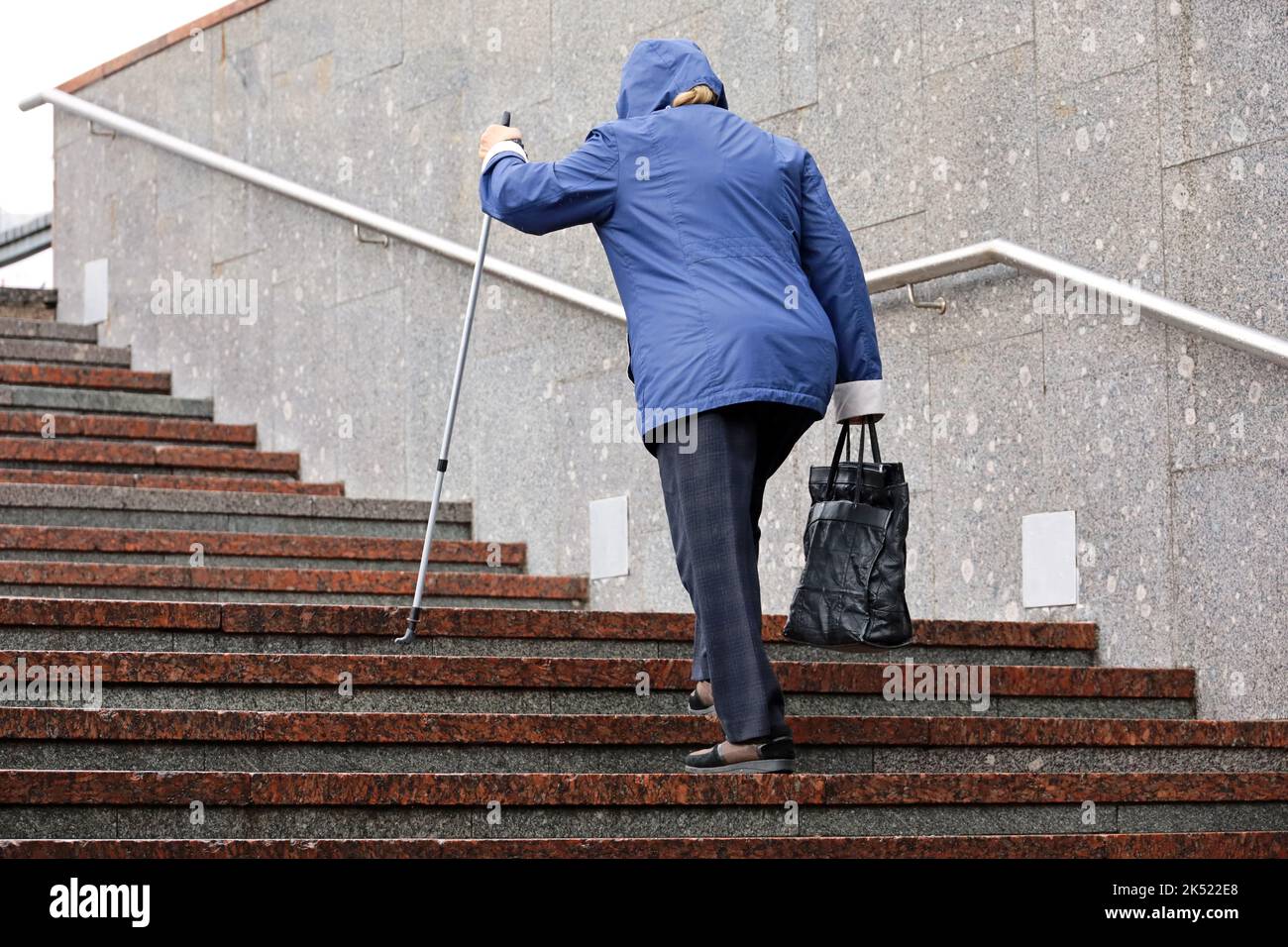 Old woman with walking cane climbing stairs outdoor. Concept for disability, limping adult, diseases of the spine Stock Photo