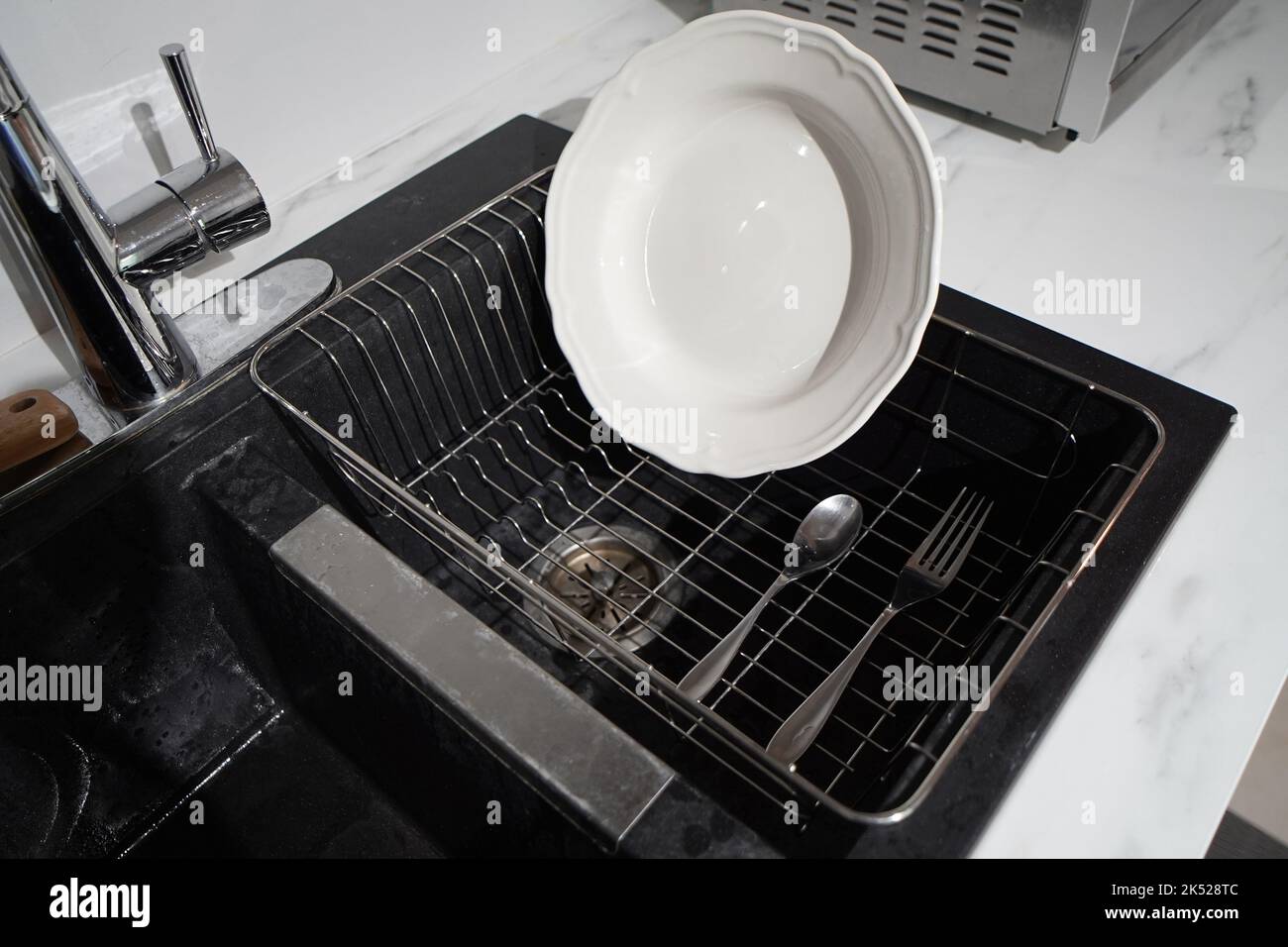 https://c8.alamy.com/comp/2K528TC/a-plate-drying-on-a-dish-rack-above-kitchen-sink-2K528TC.jpg