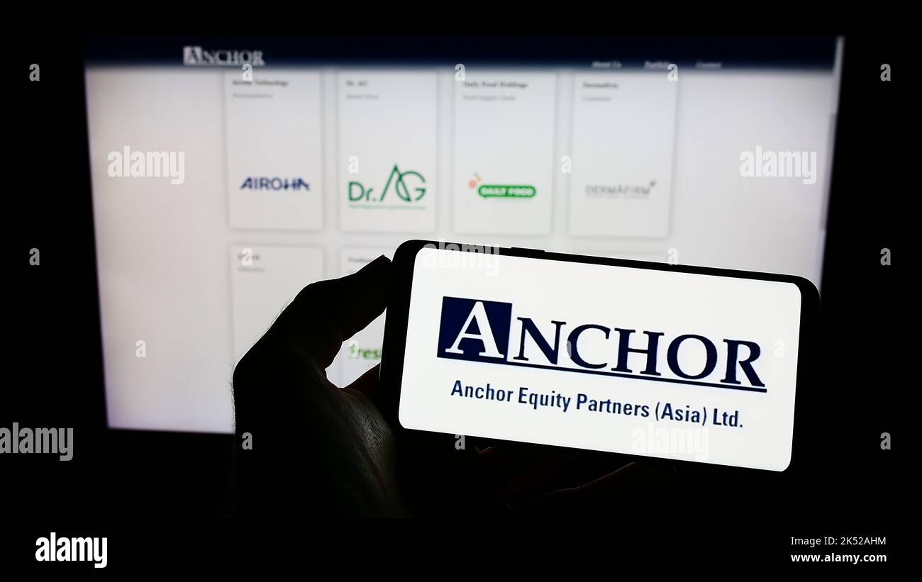 Person holding cellphone with logo of company Anchor Equity Partners (Asia) Limited on screen in front of webpage. Focus on phone display. Stock Photo