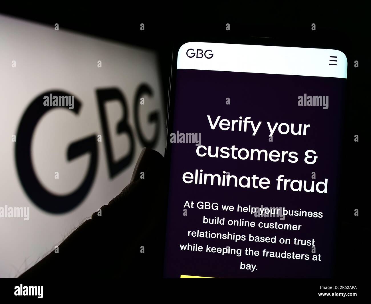 Person holding cellphone with website of identity verification company GB Group plc (GBG) on screen with logo. Focus on center of phone display. Stock Photo