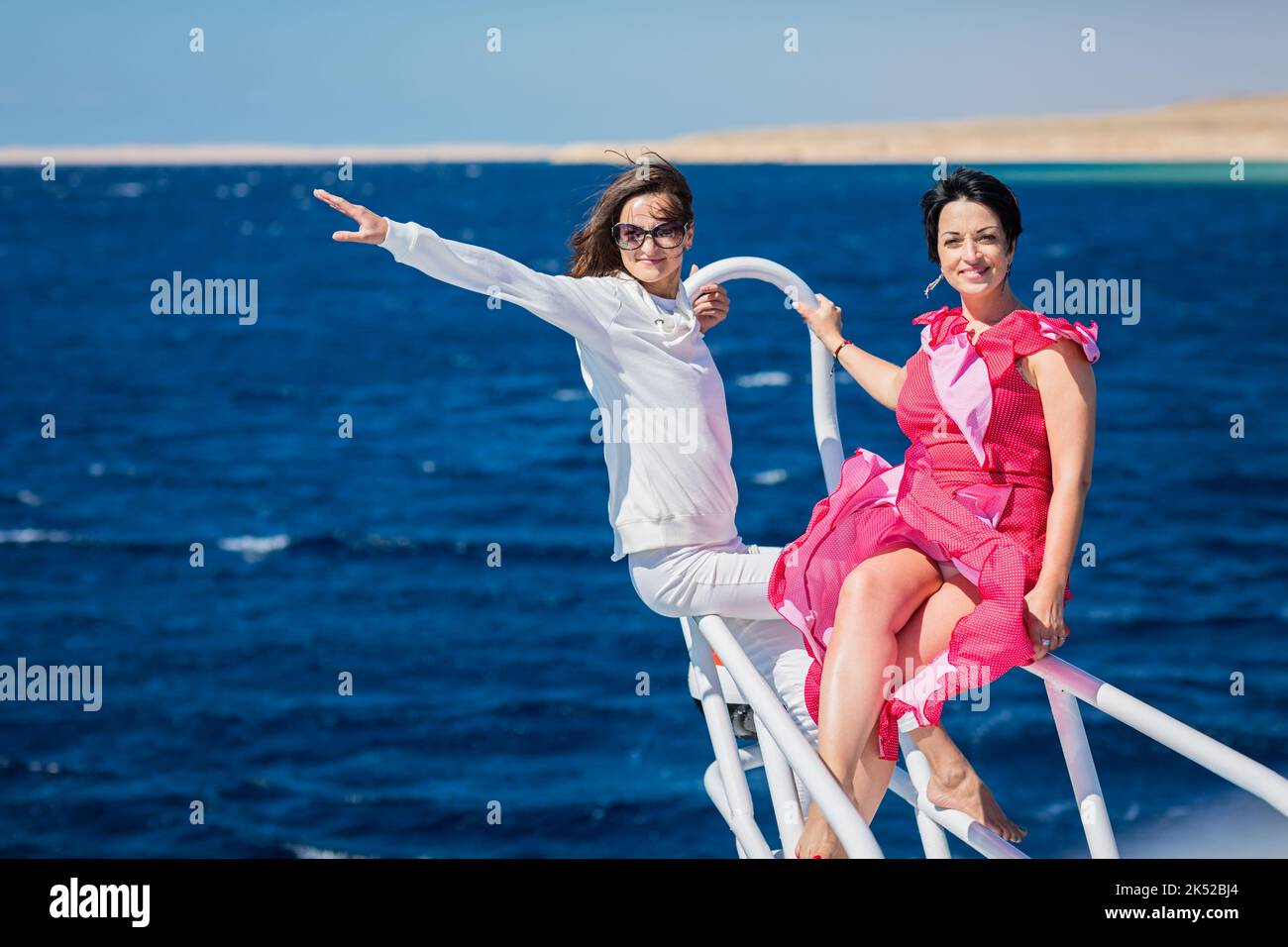 Two women relaxing together on the nose of the yacht at sunny summer day at sea Stock Photo