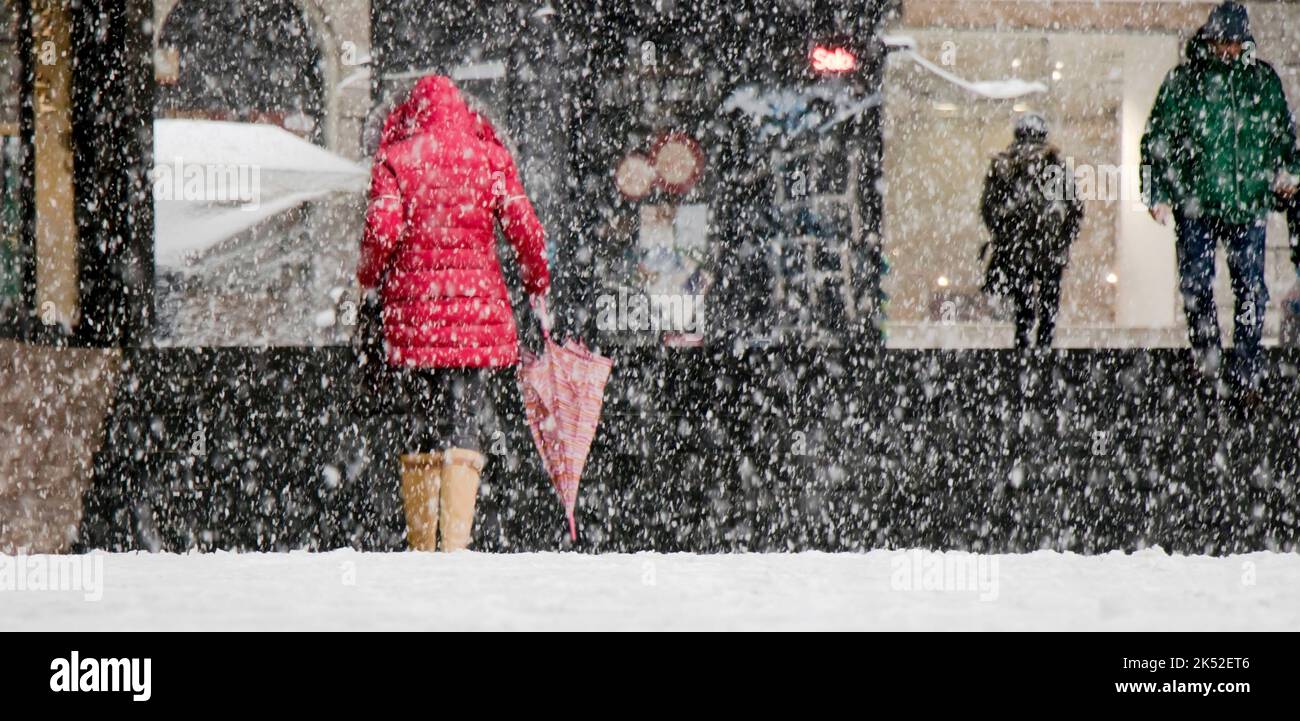 Belgrade, Serbia - December 15, 2018: Woman wearing red parka and holding umbrella and other pedestrians walking city street on a snowy day Stock Photo