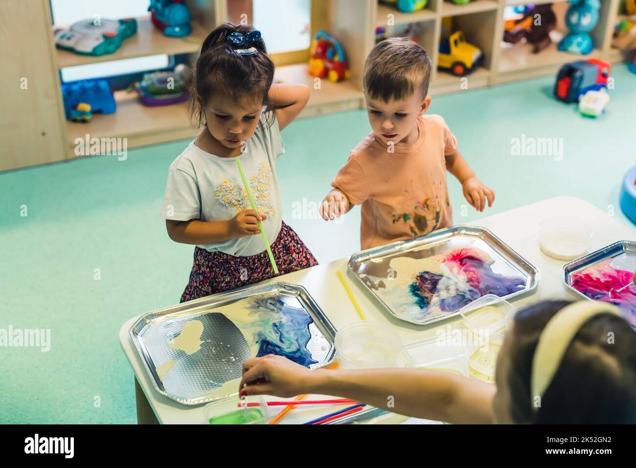 preschoolers painting using small tubes in the room full of toys, kindergarten medium shot. High quality photo Stock Photo