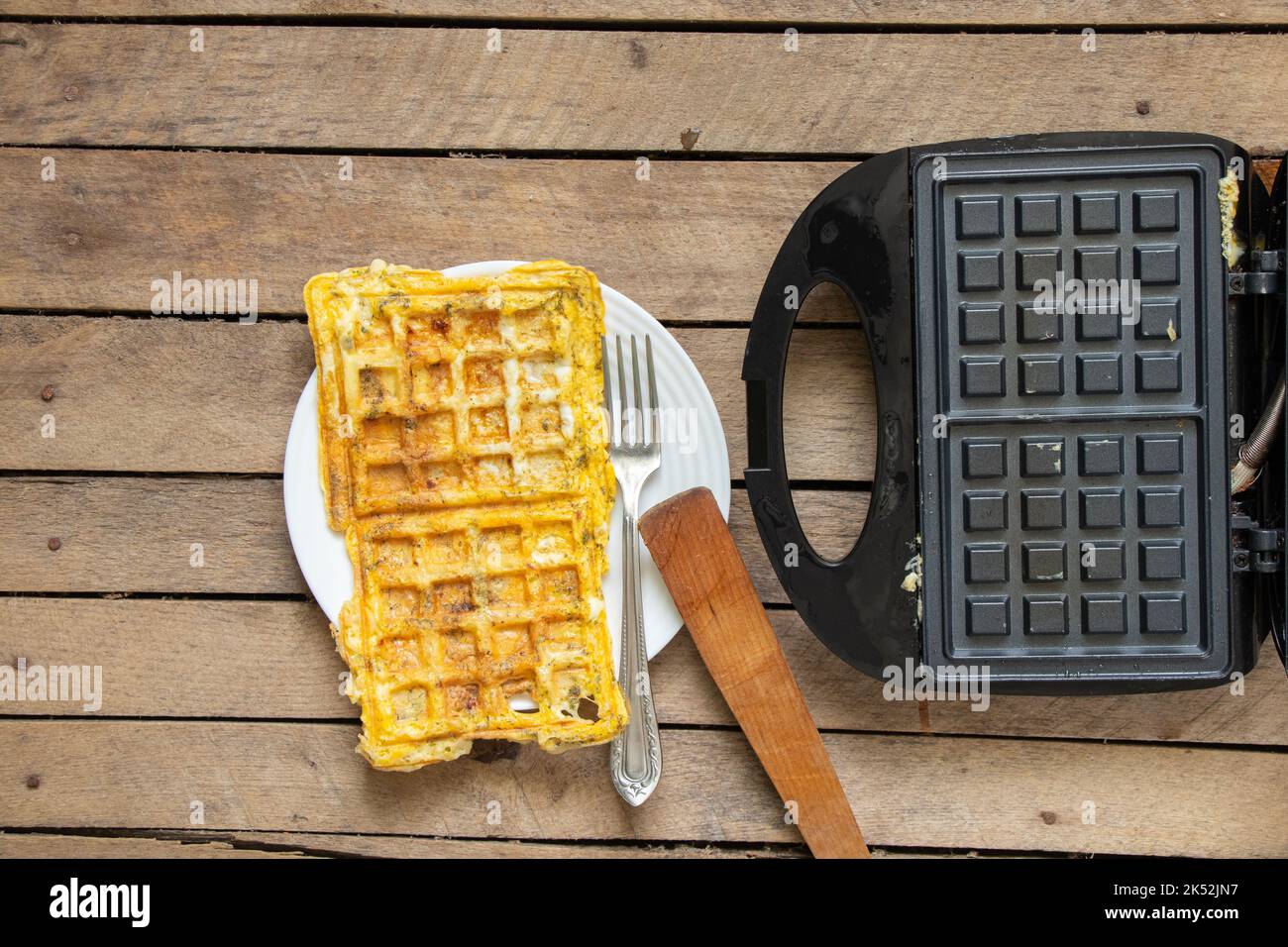 fry scrambled eggs with cheese and spices in a waffle iron on a wooden table in the kitchen, boil scrambled eggs in a waffle iron, breakfast Stock Photo