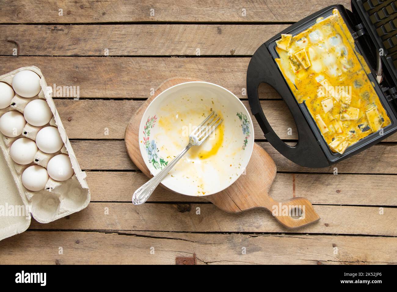 fry scrambled eggs with cheese and spices in a waffle iron on a wooden
