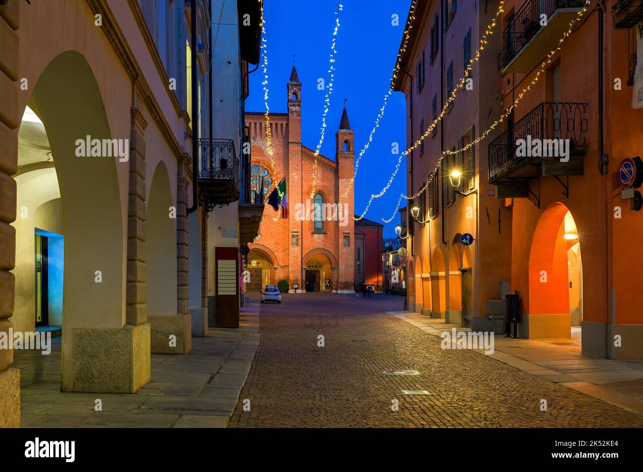 Narrow cobblestone street among old historic buildings illuminated with Christmas lights in Alba, Italy. Stock Photo