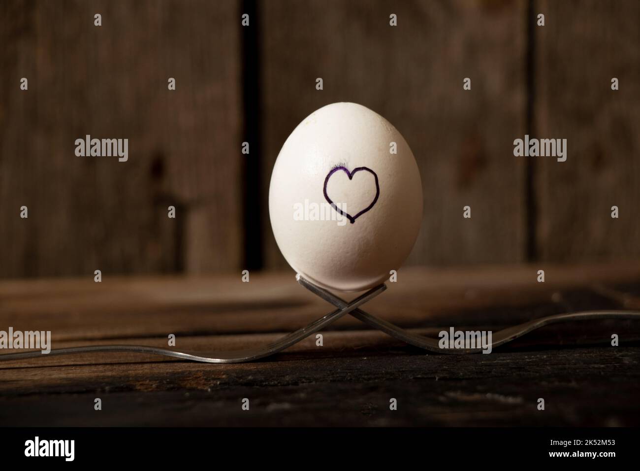 heart is drawn on a chicken egg that lies on forks on an old wooden table, love and feelings Stock Photo