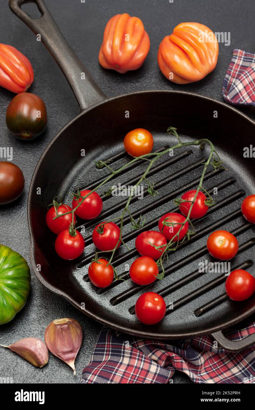 A sprig of cherry tomato in frying pan. Tomatoes and garlic cloves on