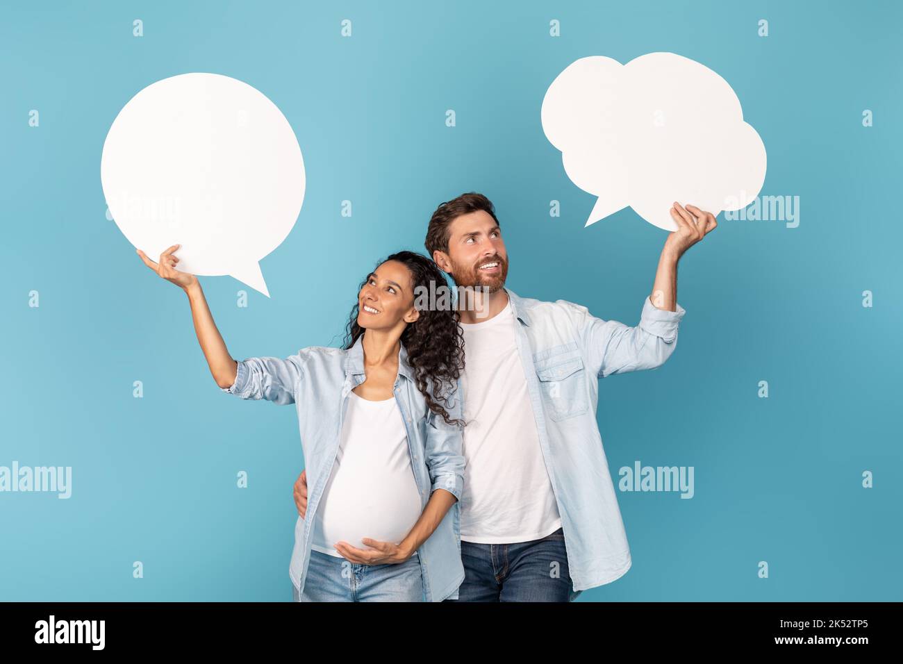 Happy young european man and arabic pregnant woman holding abstract clouds, bubbles with empty space Stock Photo