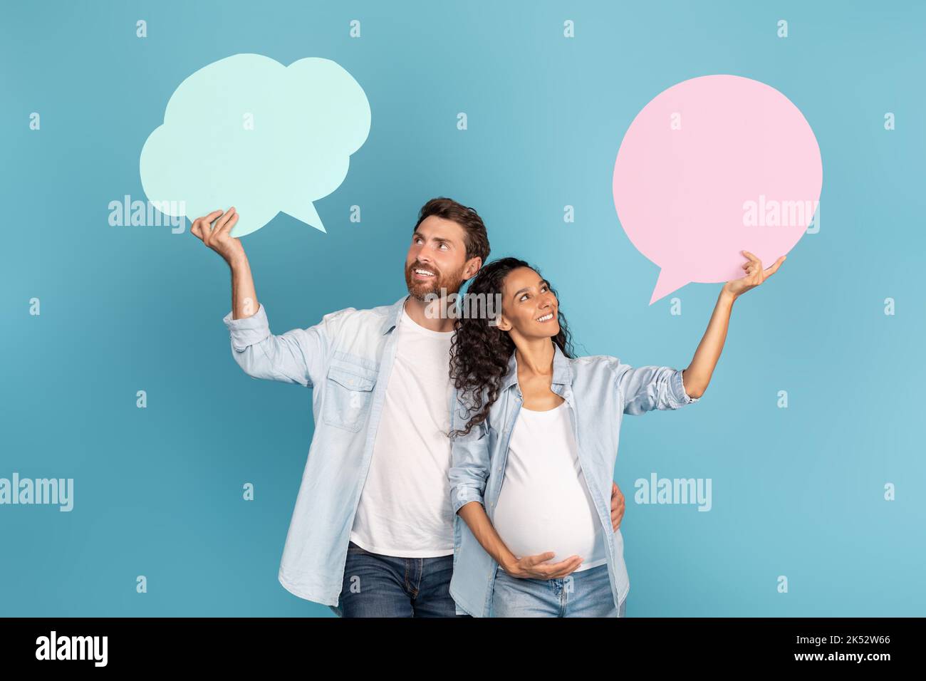 Smiling young european guy and arab pregnant lady hold abstract clouds, bubbles with empty space Stock Photo