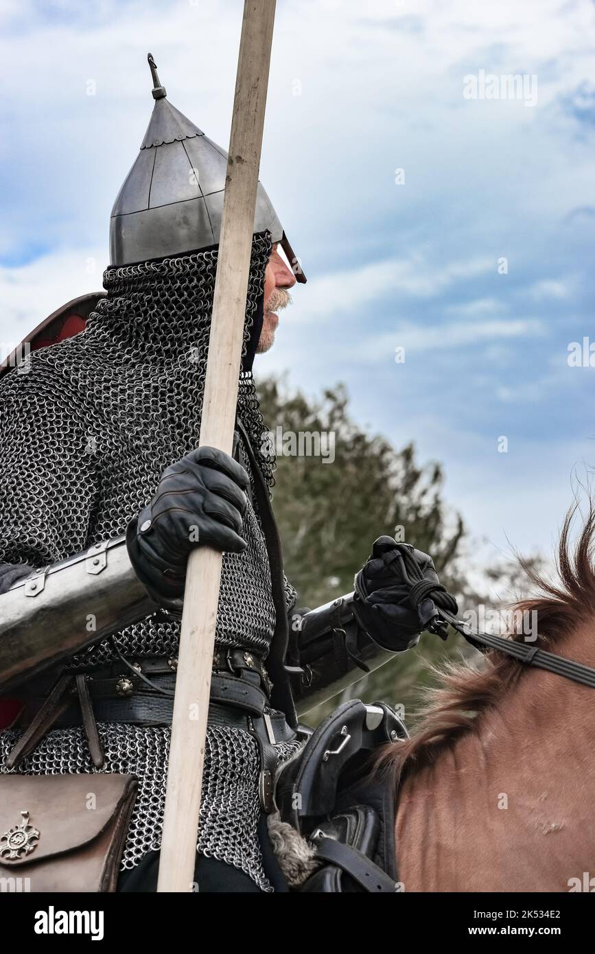 Old horseman in chain mail armor, helmet with wooden pike weapon equipped on horse blue sky Stock Photo