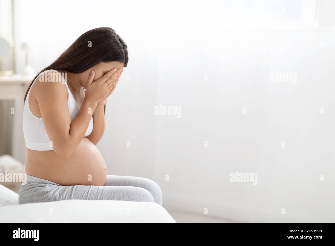 Young pregnant woman feeling sad, crying at home Stock Photo