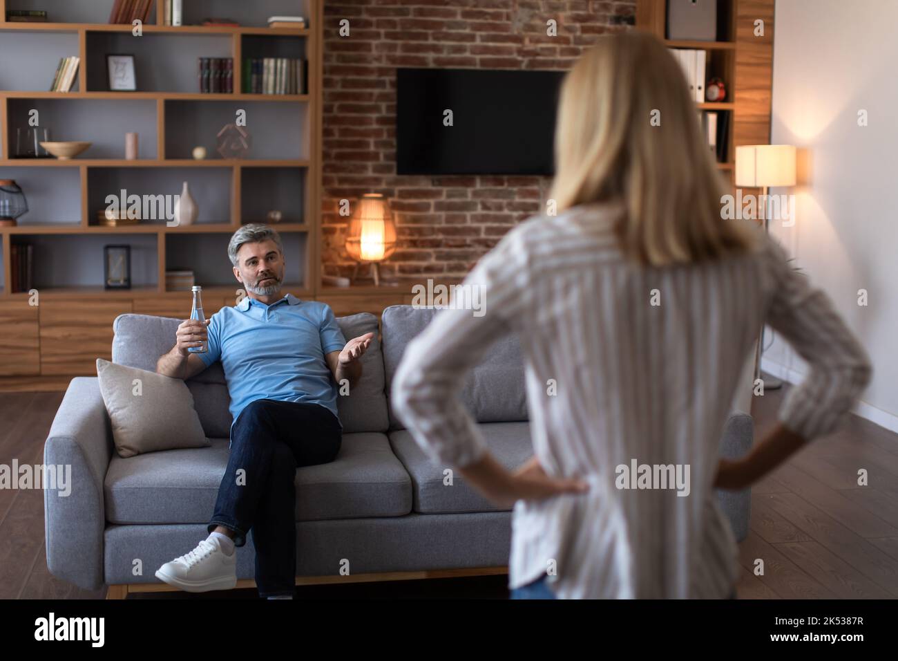 Angry mature caucasian wife scolds at husband with bottle of beer on ...