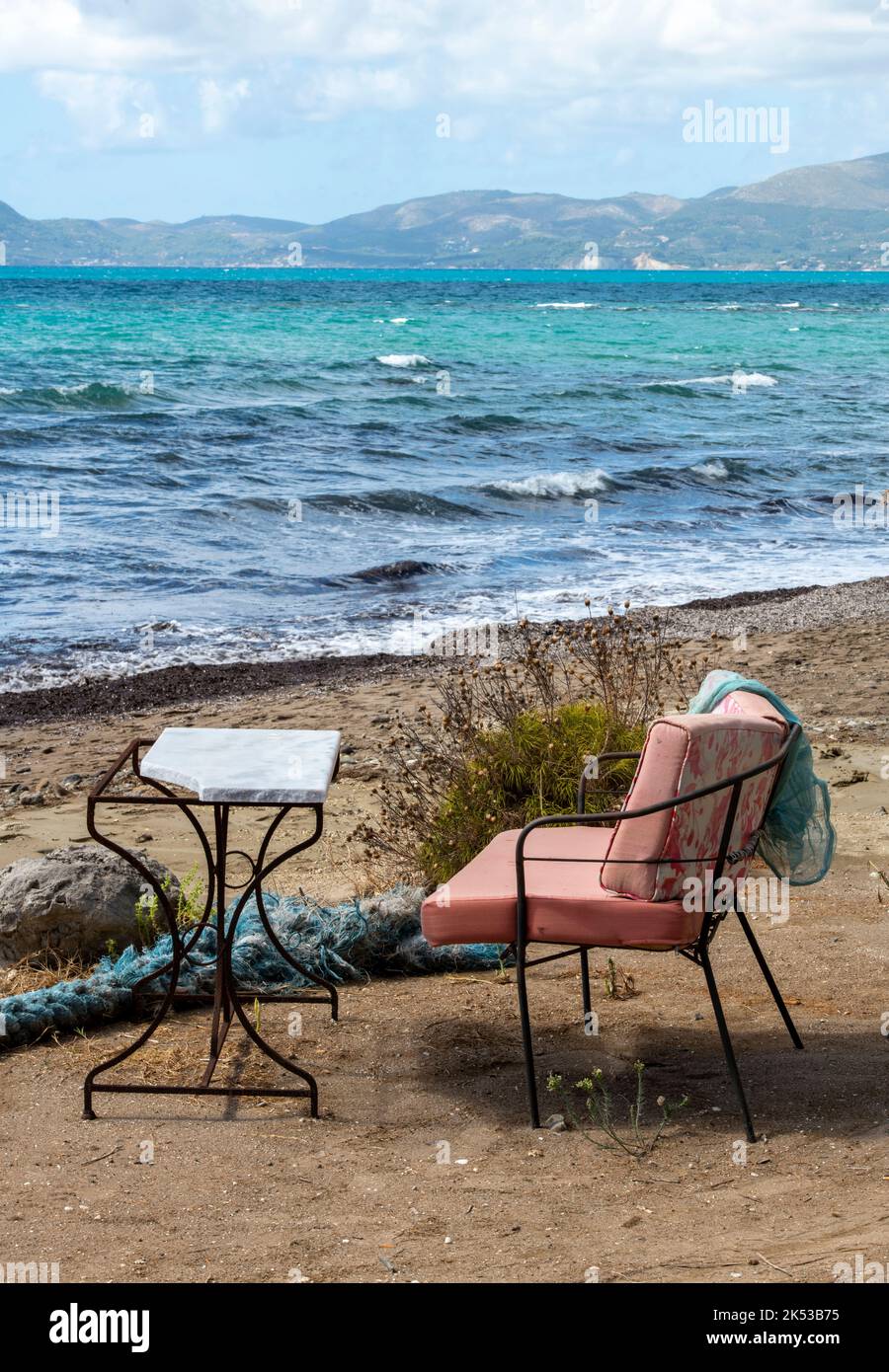 vintage table and chair on the beach at dafni on the greek island of zante or zakynthos with the sea and mountains in the background. Stock Photo