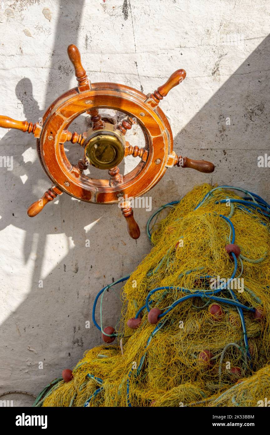 ships wheel and fishing nets on an old trawler, traditional wooden ships helm, maritime themed nets and wheel, helm and fishing nets, trawling fishing. Stock Photo