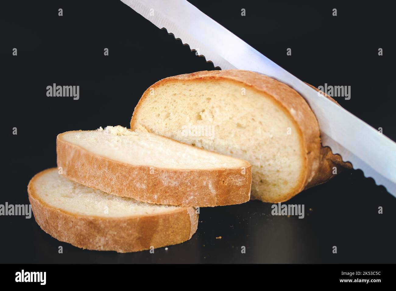 Knife slicing freshly baked loaf of bread. Dark food photo. Selective focus. Toned Stock Photo