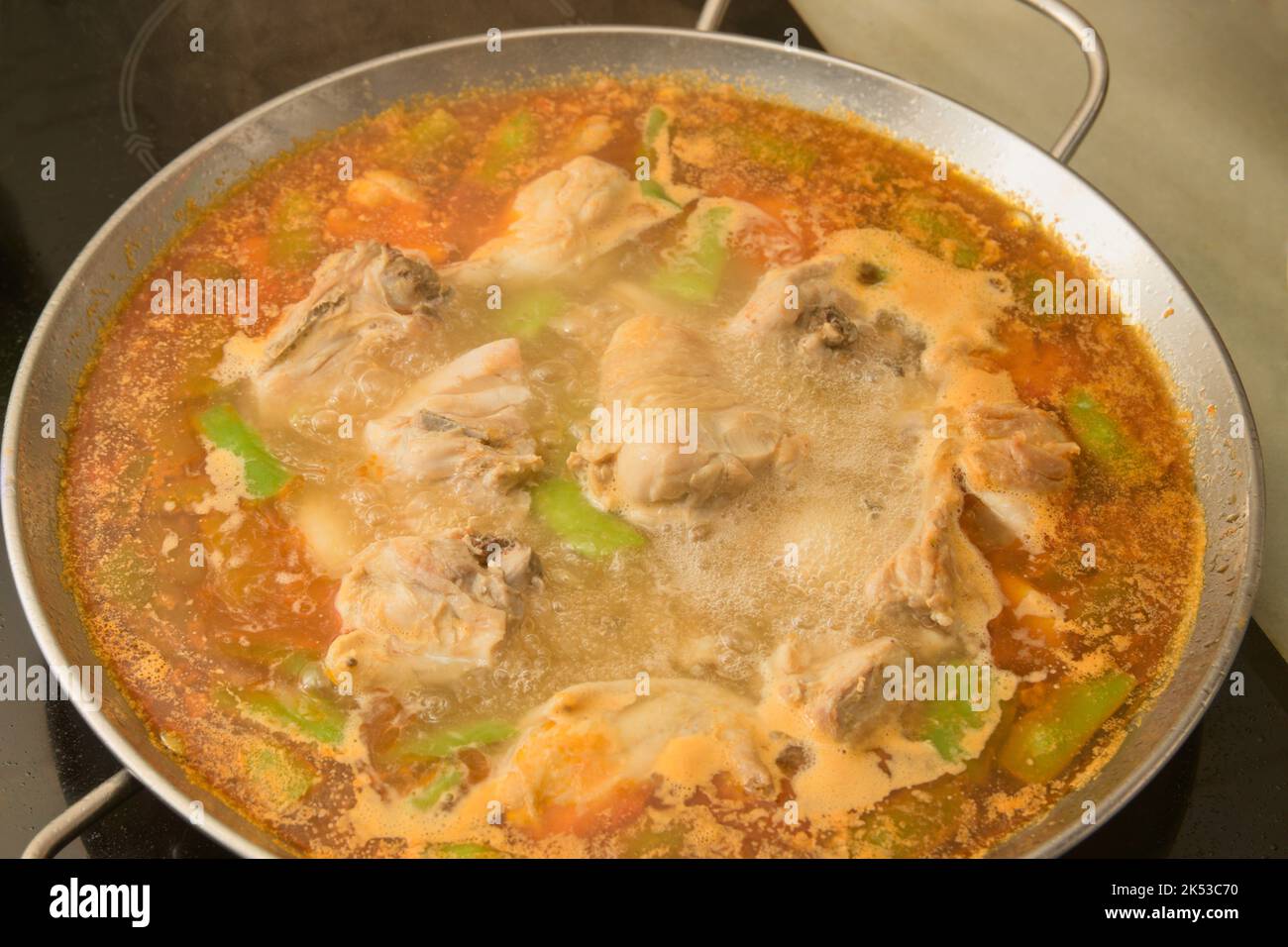 Image of a Valencian paella that is in the process of being prepared with boiling water in a homemade ceramic hob Stock Photo