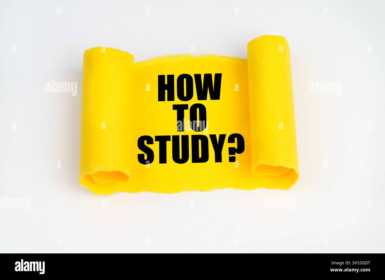 On a white surface, a yellow scroll of paper with the inscription - HOW TO STUDY. Business concept. Stock Photo