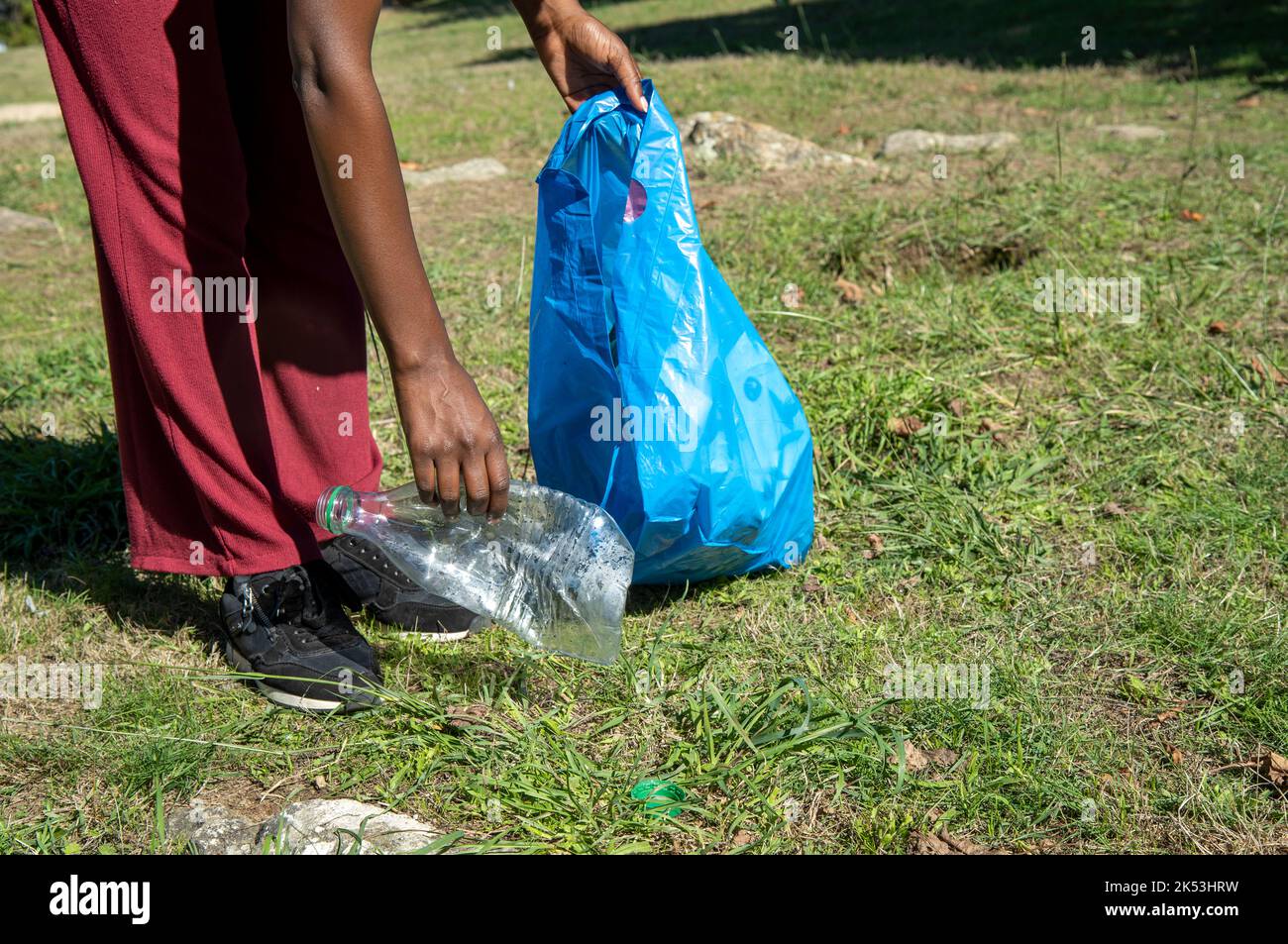 Young woman cleaning up plastics from field. Collecting garbage in a