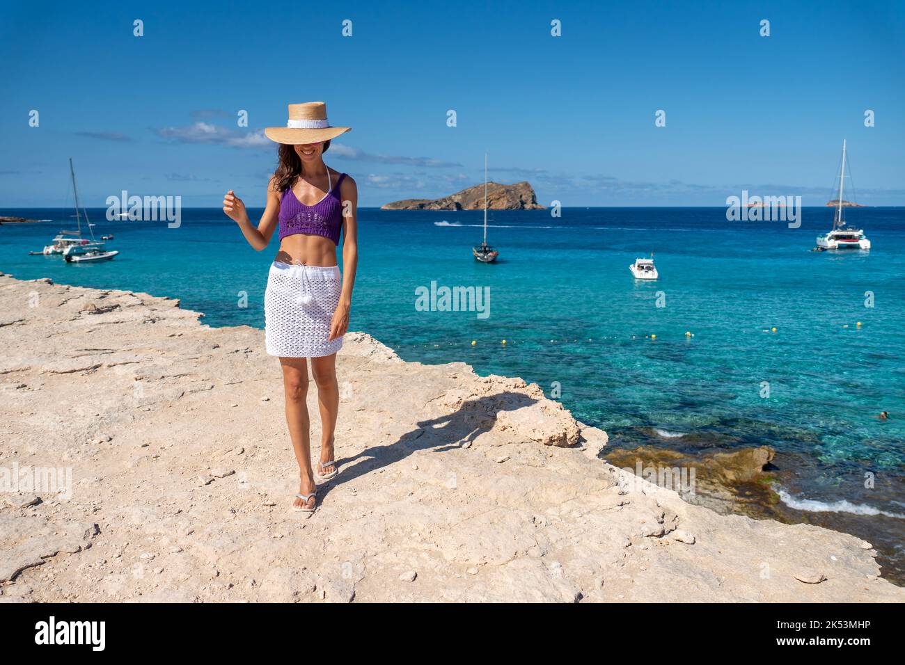 Brunette woman with hat, white skirt and purple top on the shore of the Mediterranean Stock Photo