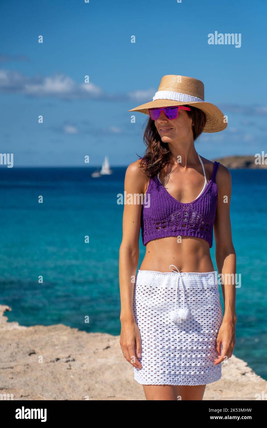 Brunette woman with hat, white skirt and purple top on the shore of the Mediterranean Stock Photo