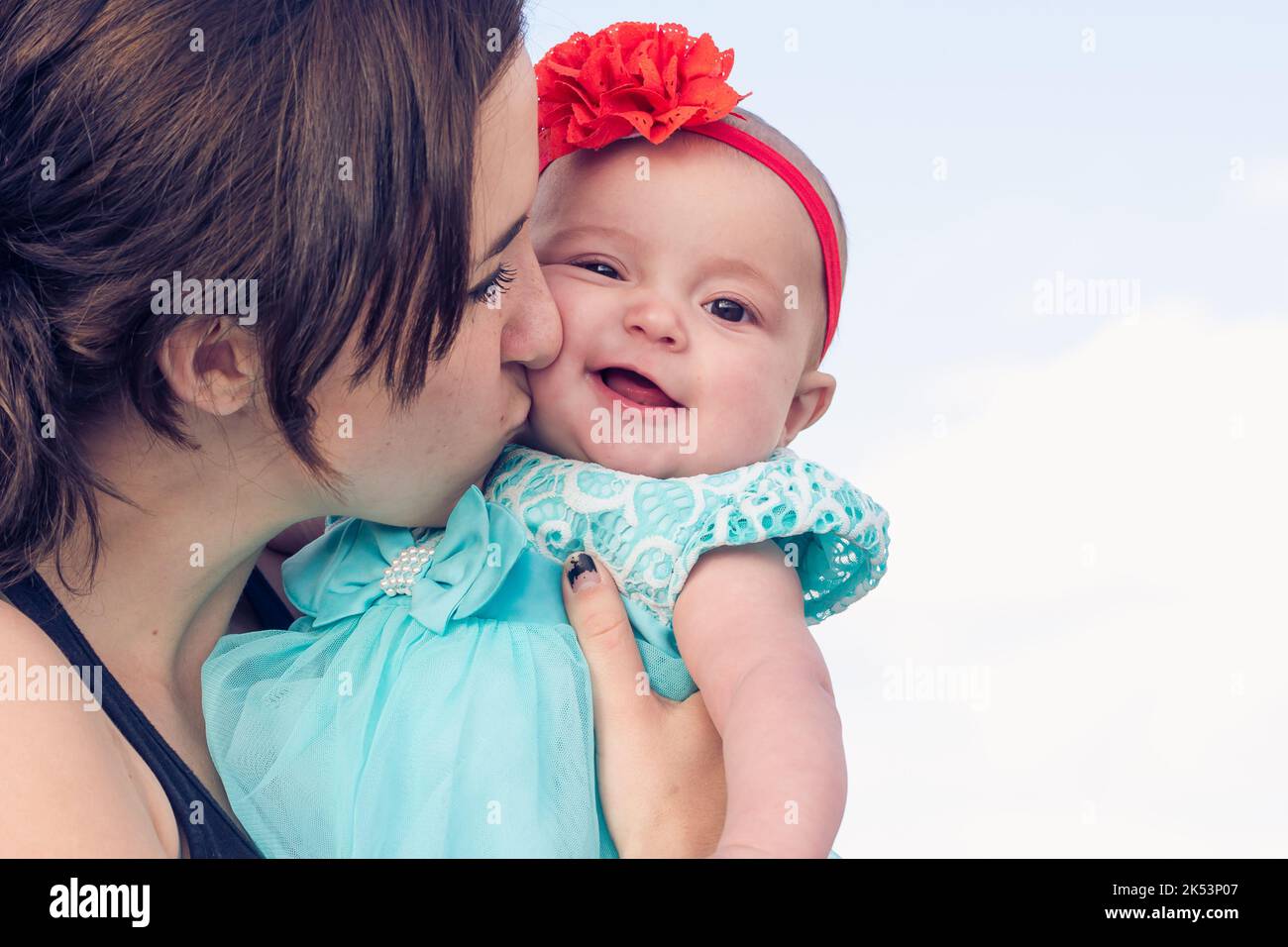 A young mother in her early twenties kisses her baby girl on the cheek. Stock Photo