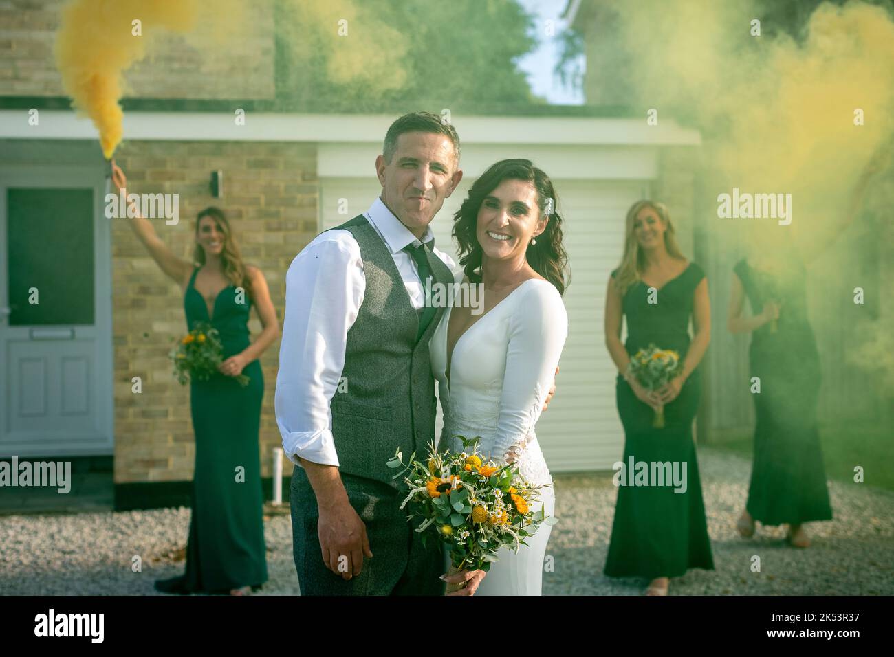 Married couple looking into lens, two bridesmaids holding flares and the third is looking on, I did a couple looking in the camera bridesmaids with flowers looking on Stock Photo