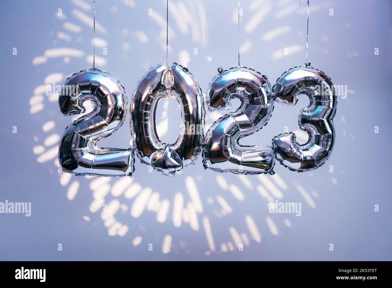 Silber foil balloons in numbers shape 2023 hanging against blue wall with fireworks projection. New Year holidays Stock Photo