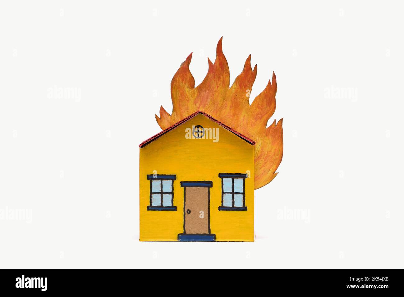 A yellow and red toy cardboard house with its roof on fire in the middle of frame isolated on a white background, captured in a studio Stock Photo