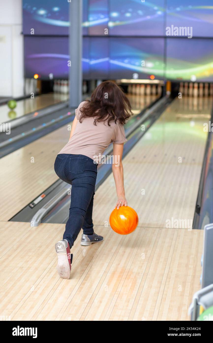 A woman throws a ball into a bowling alley. Paths with balls and pins for bowling. A fun game