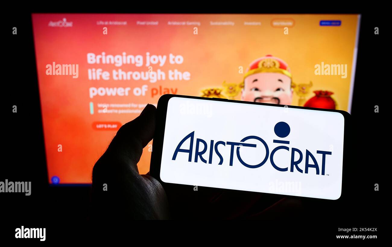 Person holding smartphone with logo of gambling company Aristocrat Leisure Limited on screen in front of website. Focus on phone display. Stock Photo