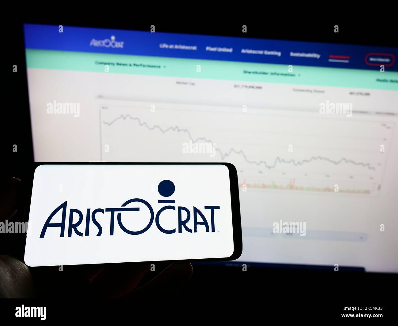 Person holding mobile phone with logo of gambling company Aristocrat Leisure Limited on screen in front of web page. Focus on phone display. Stock Photo