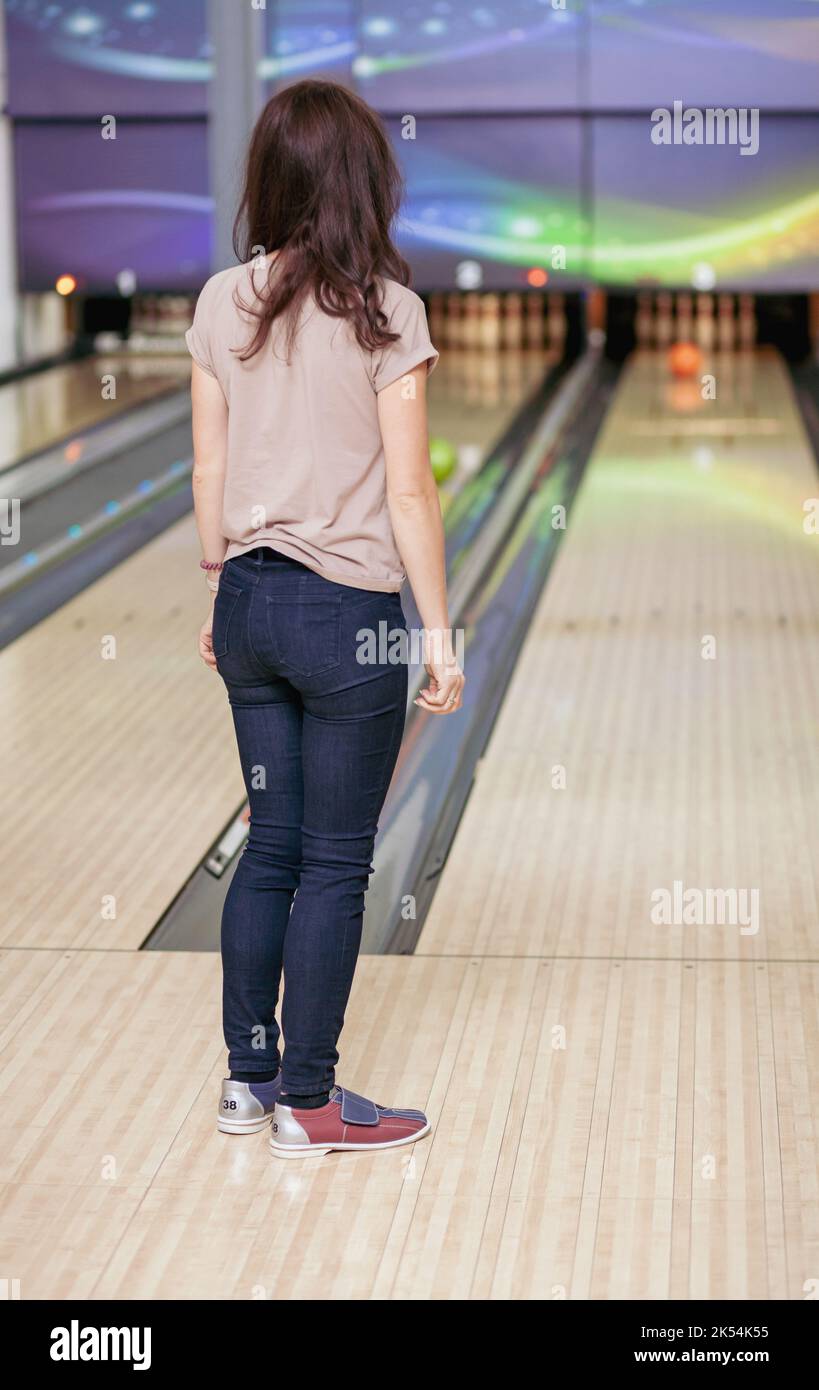 A woman throws a ball into a bowling alley. Paths with balls and pins for bowling. A fun game