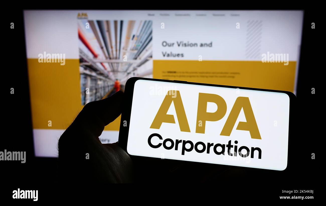 Person holding cellphone with logo of US petroleum company APA Corporation on screen in front of business webpage. Focus on phone display. Stock Photo