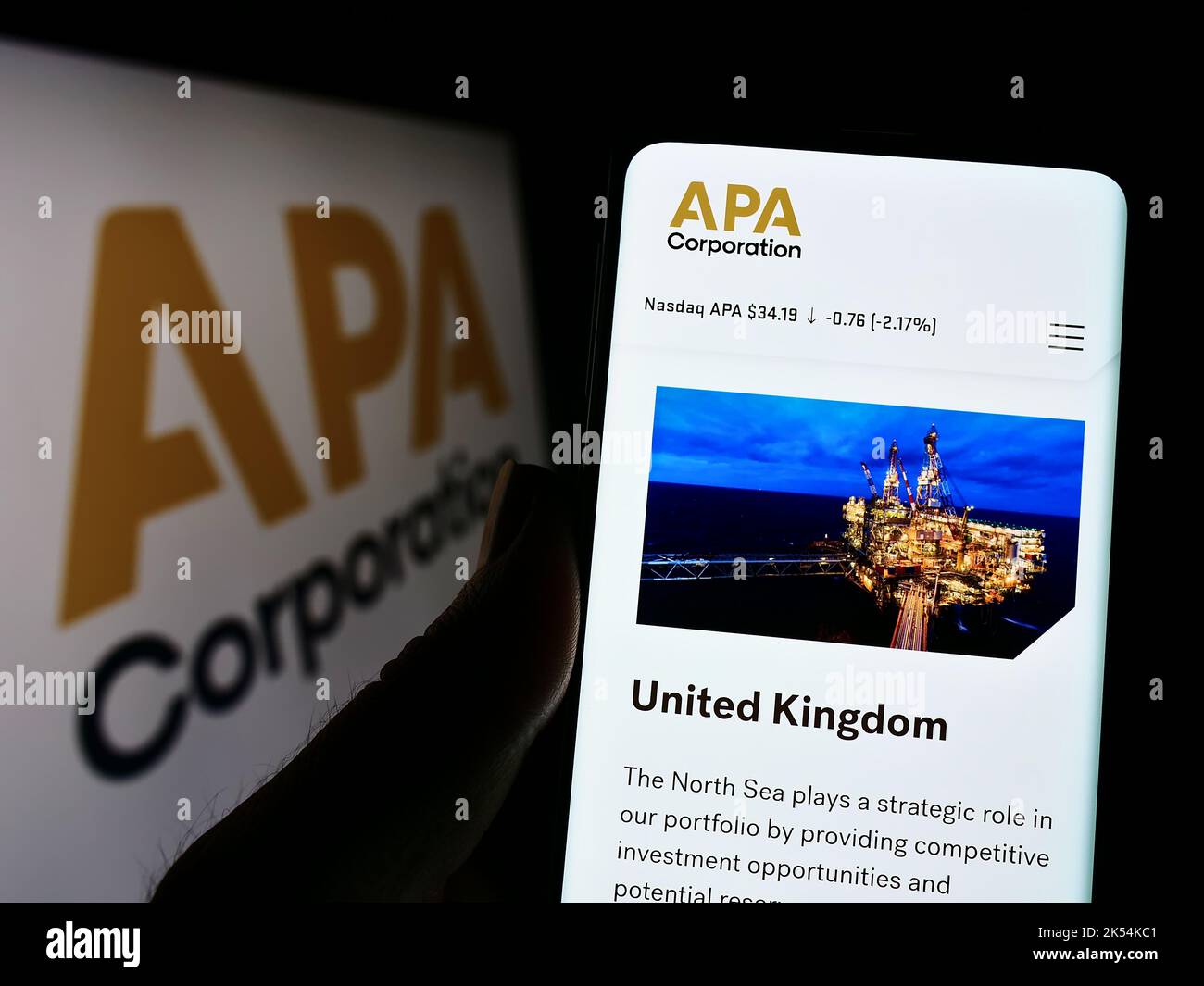 Person holding cellphone with webpage of US petroleum company APA Corporation on screen in front of logo. Focus on center of phone display. Stock Photo