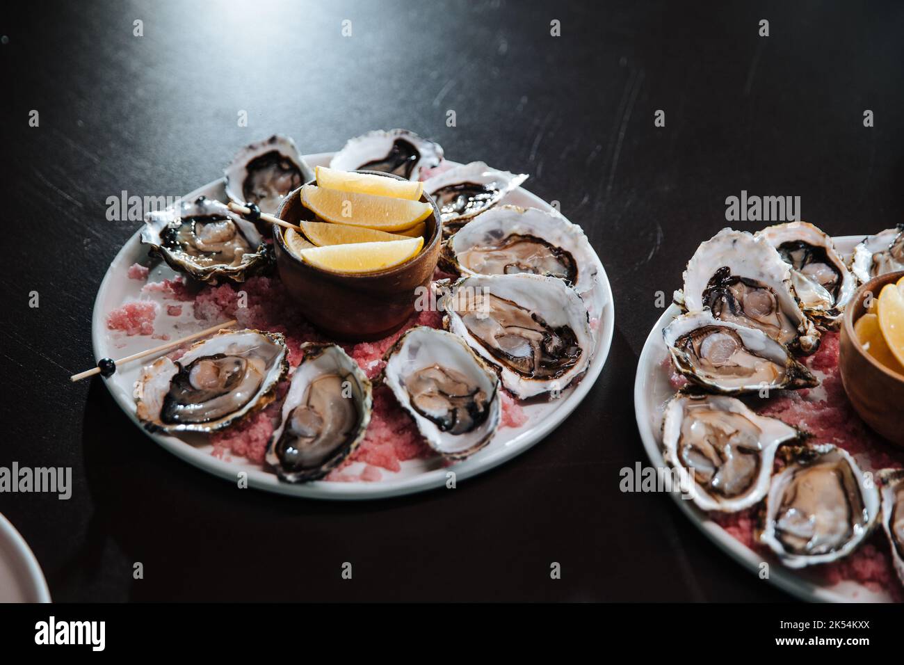 Opened Oysters on a white plate with lemon on dark wooden background, seafood, mollusk, luxury. Stock Photo