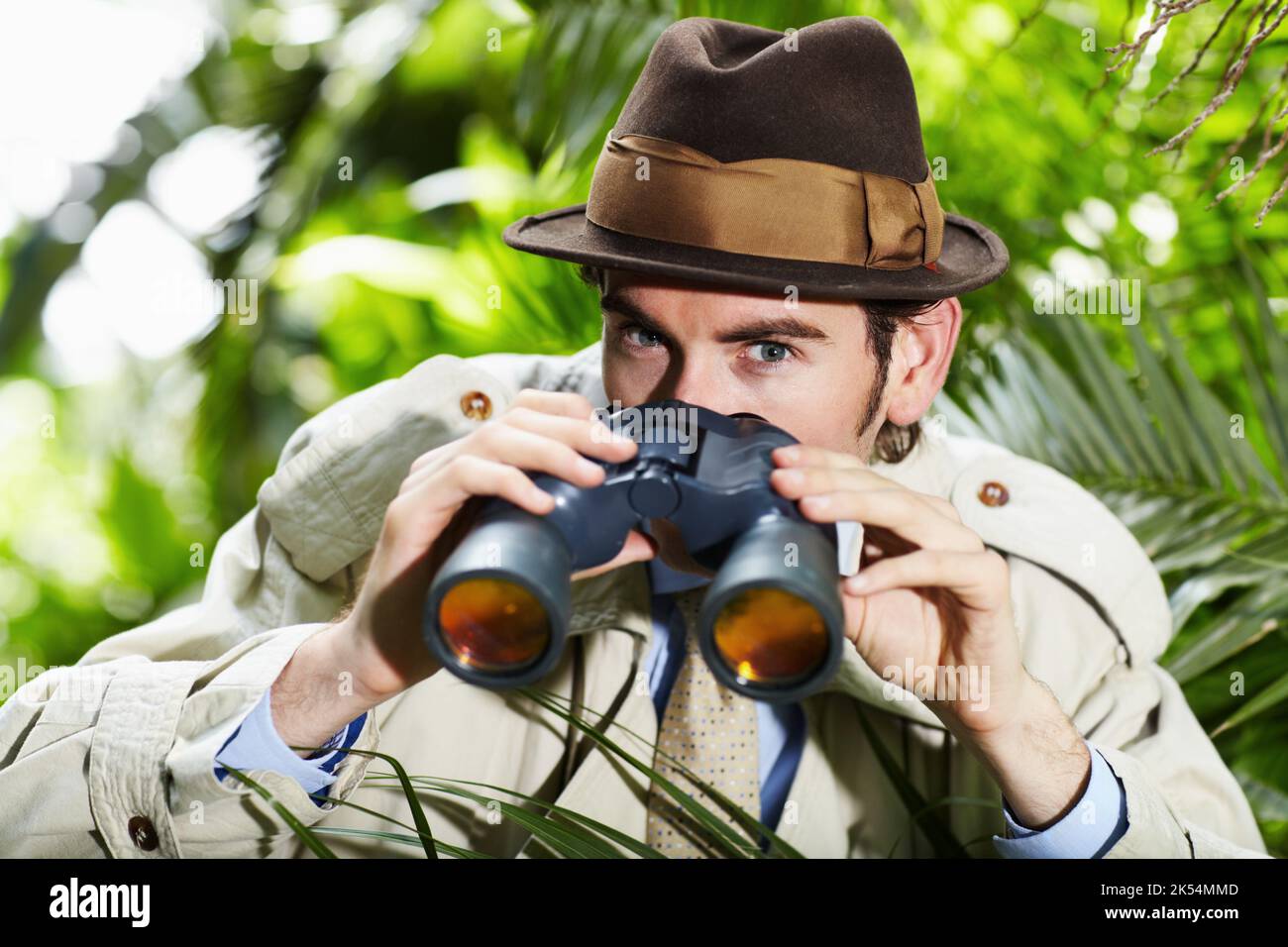 He doesnt miss a thing. Private investigator using binoculars to spy on someone from the bushes. Stock Photo