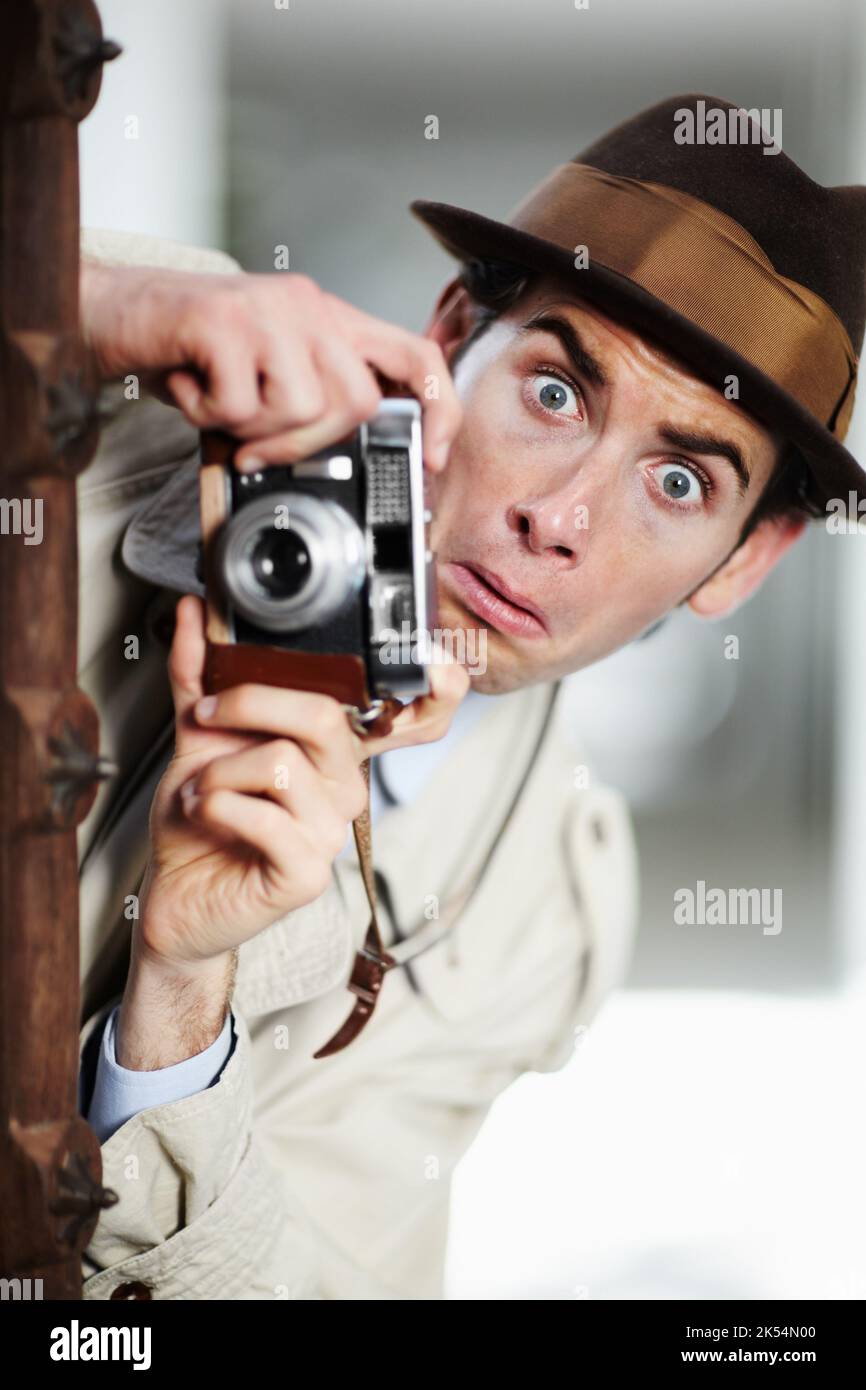 Oops, theyve seen me. Private detective capturing a photo suspiciously from around a corner while using a retro camera. Stock Photo