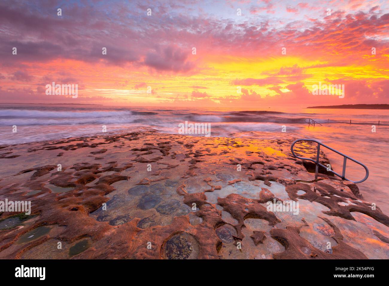Incoming waves overflow onto the eroded rockshelf and rockpool  with amazing  sunrise sky full of colours Stock Photo