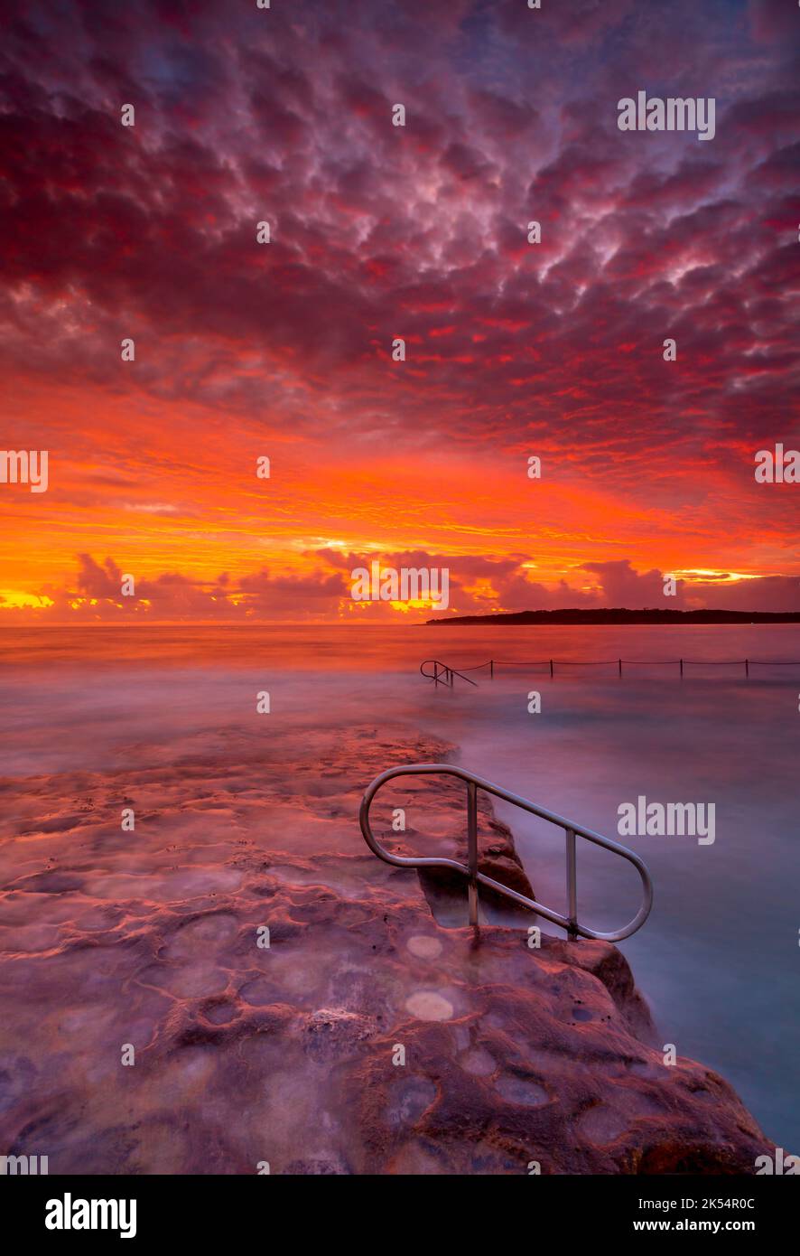 Rich red stunning sunrise over rock pool and ocean in Cronulla Stock Photo