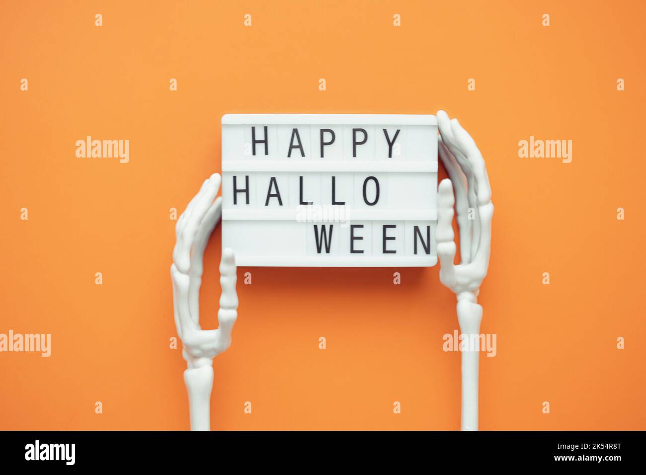 Lightbox with the inscription HAPPY HALLOWEEN in the hands of a skeleton on an orange background.  Stock Photo