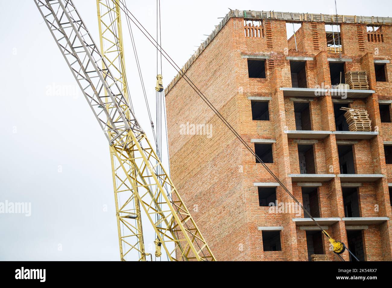 Big yellow construction crane on a background of a brick house. The