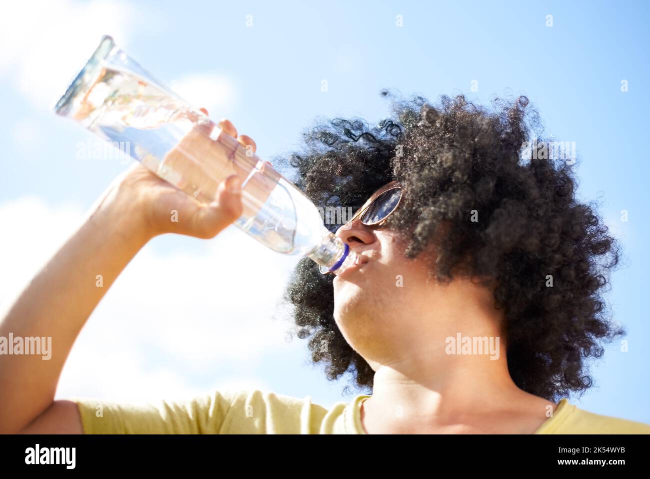 Sipping in the sun. a young man with a black afro wig drinking out of a bottle. Stock Photo