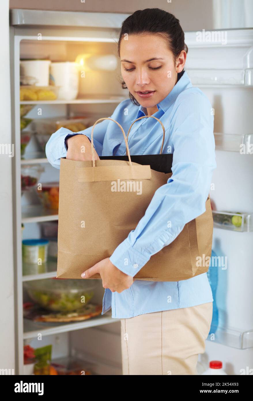 Daily homely duties. a young woman packing groceries into the fridge ...