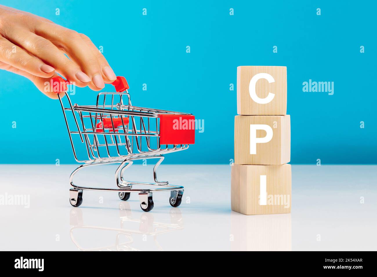 CPI - Consumer Price Index symbol.Letter block in word CPI abbreviation of consumer price index and woman's hand pushing empty shopping cart on blue b Stock Photo