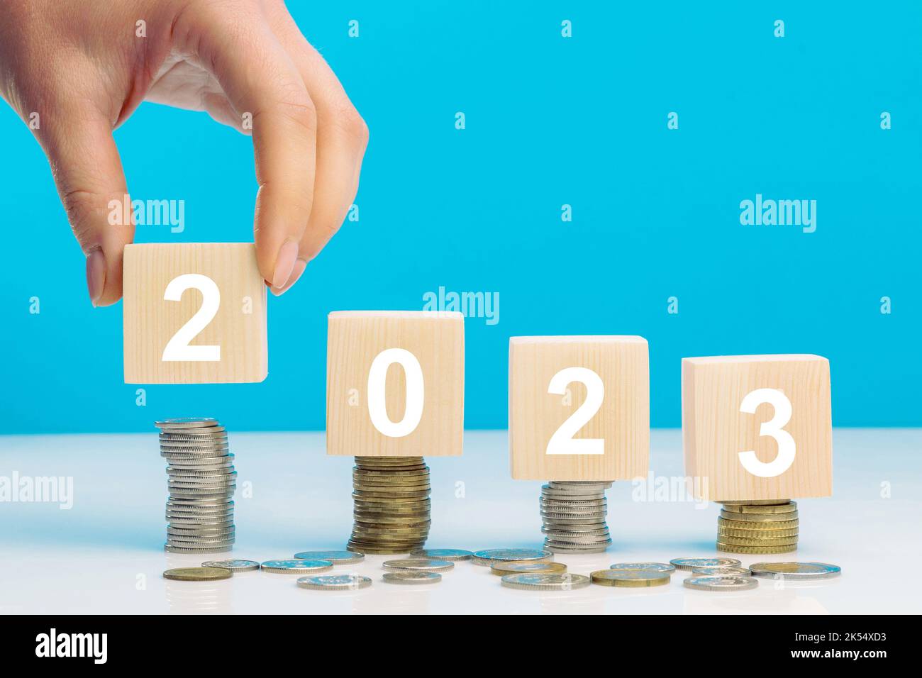 Hand place wooden cube 2023 with stack of coins with blue background ...
