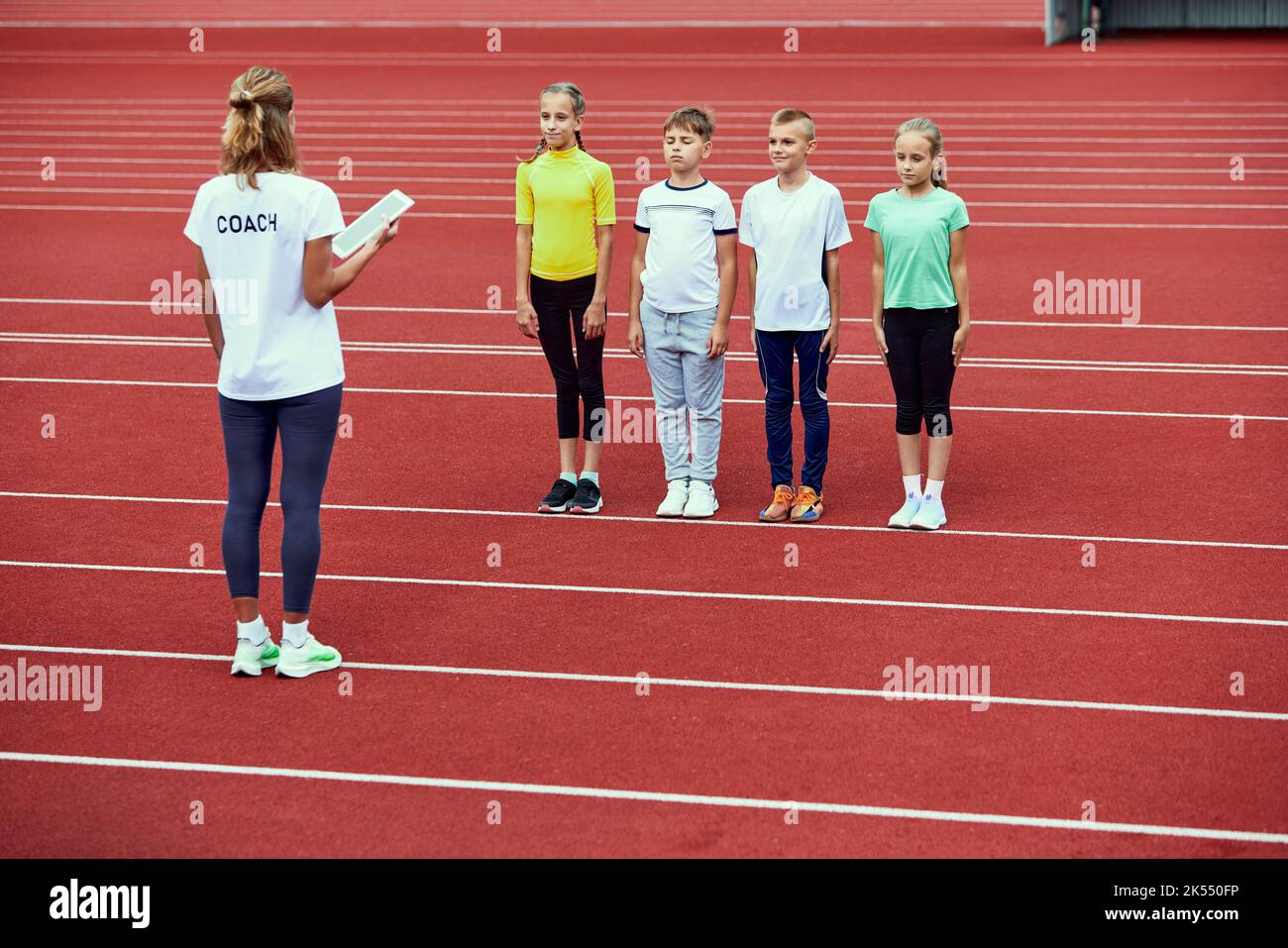 Female coach training beginner athletes. Group of children before running on treadmill at the stadium. Concept of sport, achievements, studying, goals Stock Photo