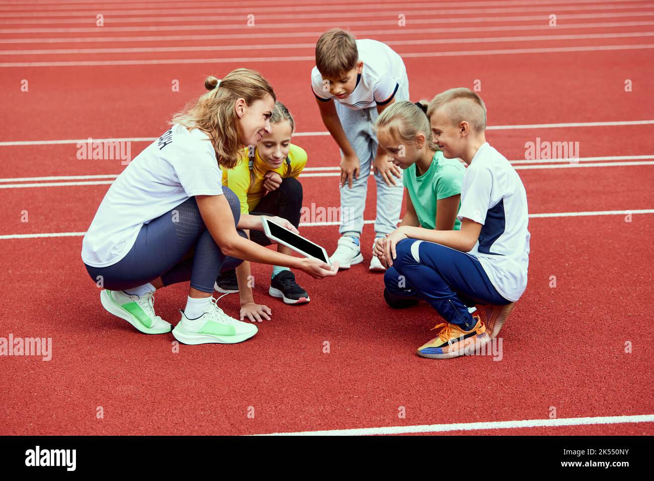 Female coach training athletes. Group of children before running on treadmill at the stadium. Concept of sport, achievements, studying, goals, skills Stock Photo