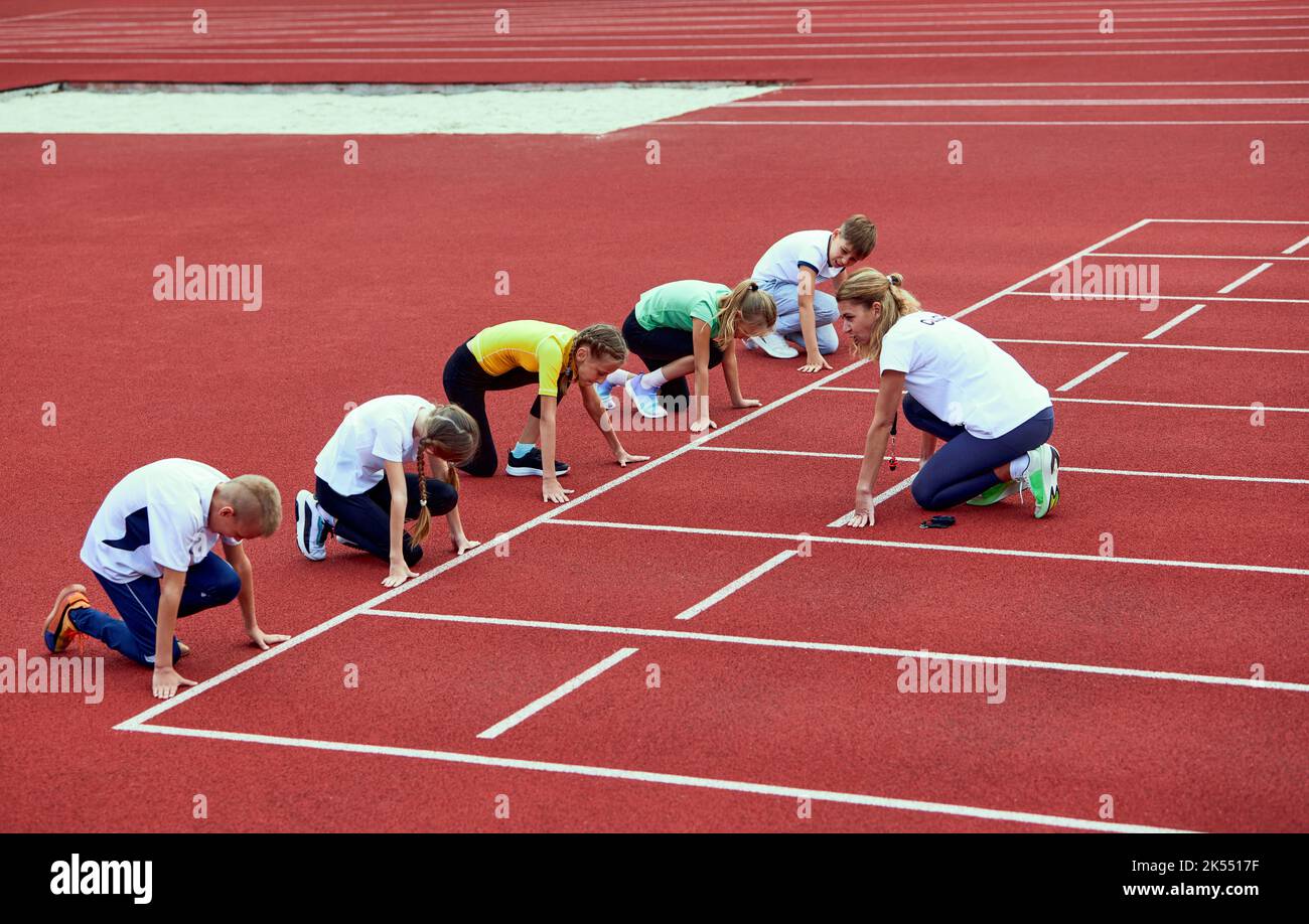 Female coach training athletes. Group of children running on treadmill at the stadium. Concept of sport, achievements, studying, goals, skills. Little Stock Photo