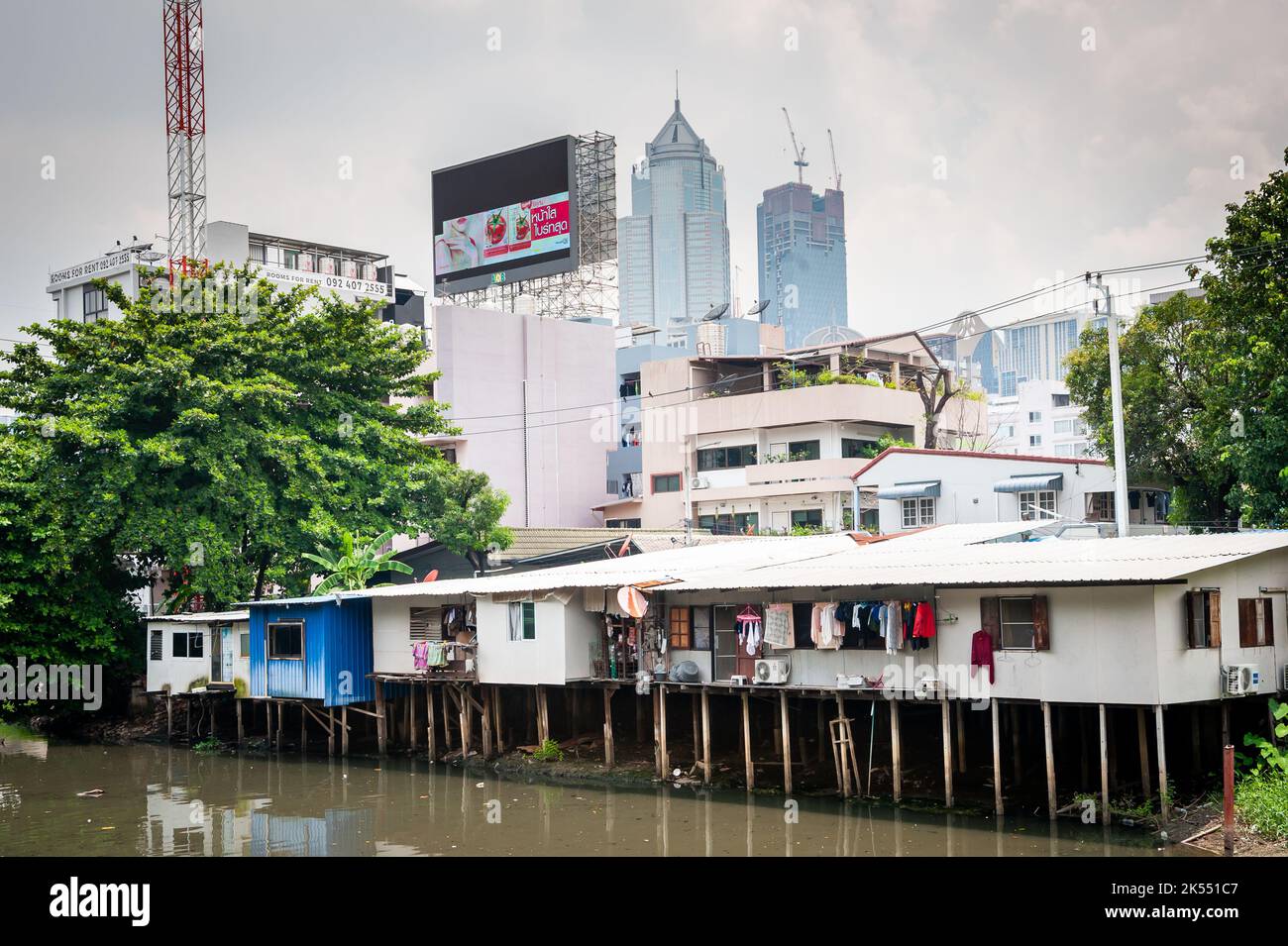 Traditional old Thai houses on stilts above a river contrast against modern high rise sky scrapers in the Soi Ruamrudee Community, Bangkok, Thailand. Stock Photo